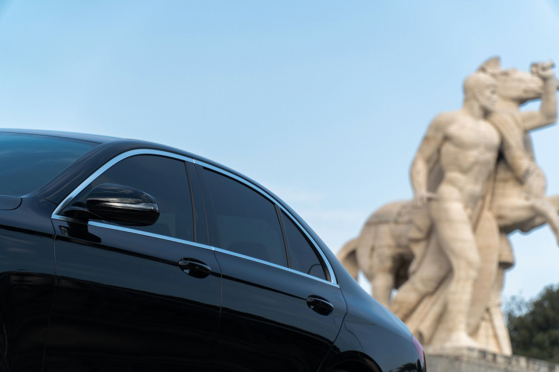Berlina nera con autista davanti a una statua in marmo