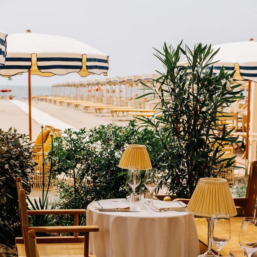 Tavolo apparecchiato sulla spiaggia tra ombrelloni a righe